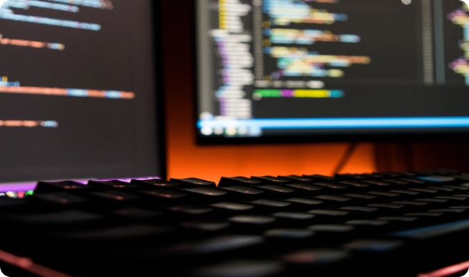 Code on monitors above a backlit keyboard